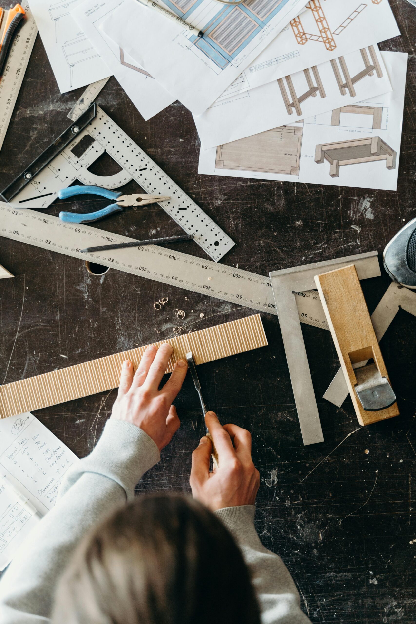 Top view of craftsman using tools and plans for woodworking indoors.